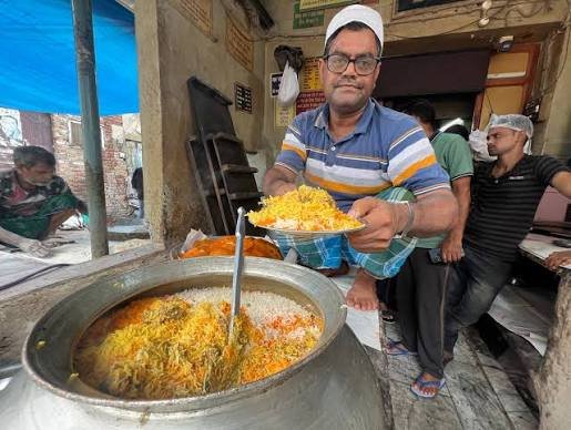 Chef preparing traditional Awadhi dum biryani in a large copper handi inside the historic Chowk kitchen in Lucknow.